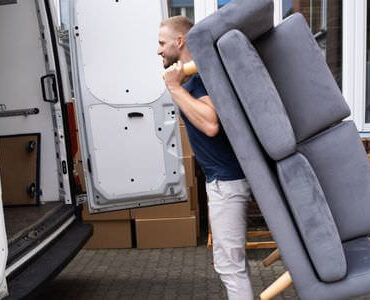 Möbellift Weinheim Möbellift Weinheim: Helfer tragen ein graues Sofa aus einem Transporter